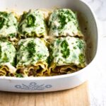 Lasagne rolls stuffed with mushrooms and topped with green sauce in a white and blue corning ware casserole dish.