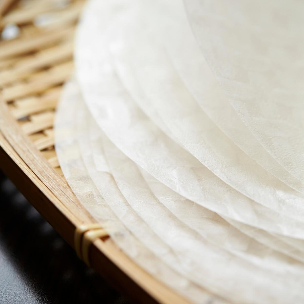 Pile of round rice paper wrappers on a bamboo tray.