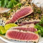 Deep purple slices of rare ahi tuna coated in white and black sesame seeds with greens in the background.