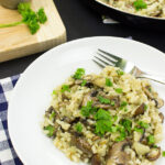 Creamy white risotto topped with cooked sliced mushrooms and green herbs in a white bowl.