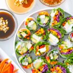 Colorful slices of vegetarian rice paper rolls with 3 bowls with different dipping sauces shown.