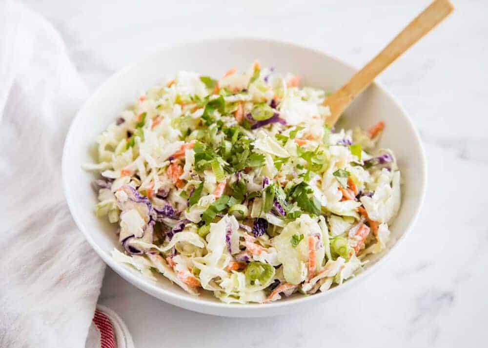 White bowl of classic coleslaw in pale green and orange shreds with chopped parsley on top. 