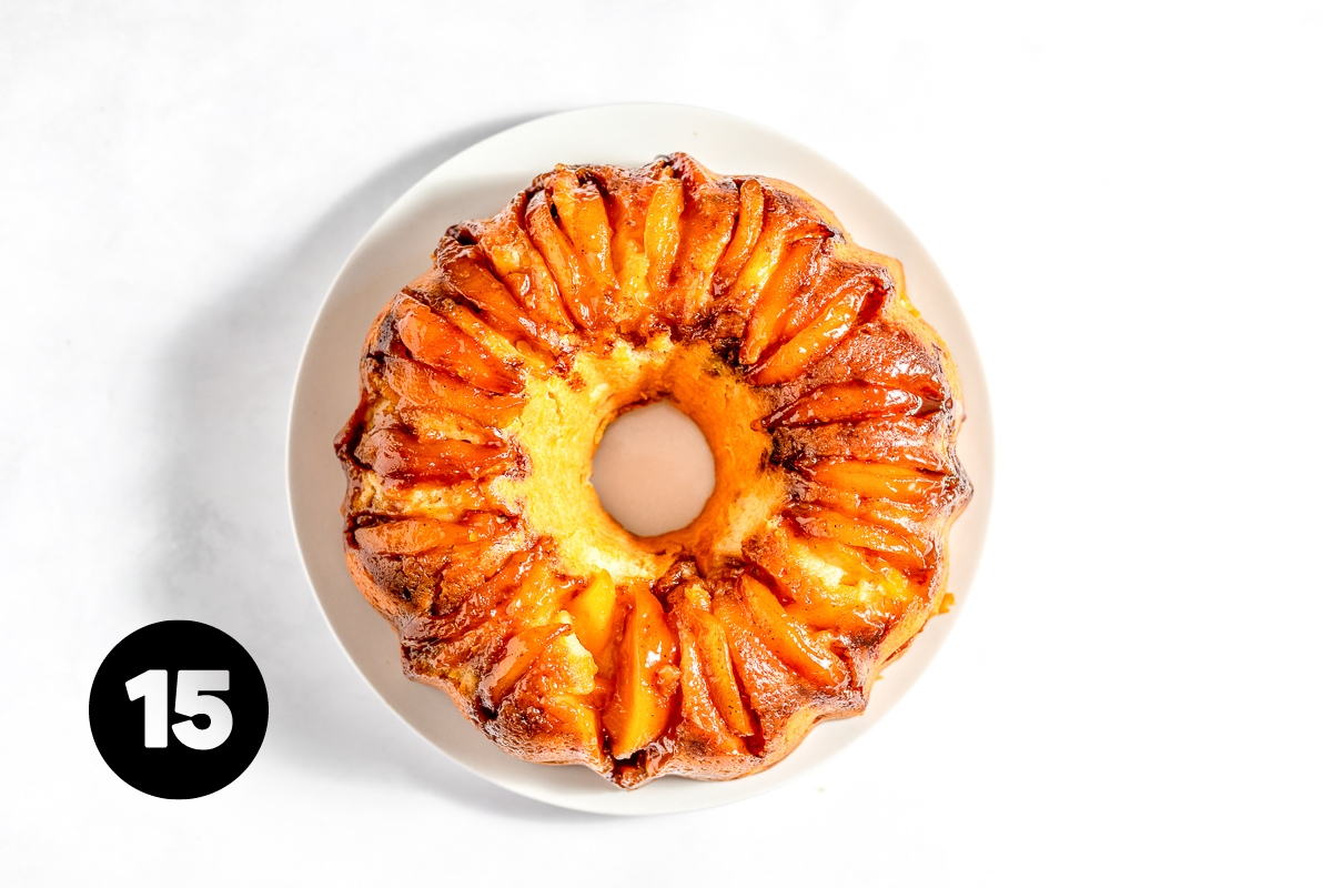 Peach cake has been inverted onto a plate and the pan removed. The cake shows the peach slices in a circle, arranged side by side around what is now the top.