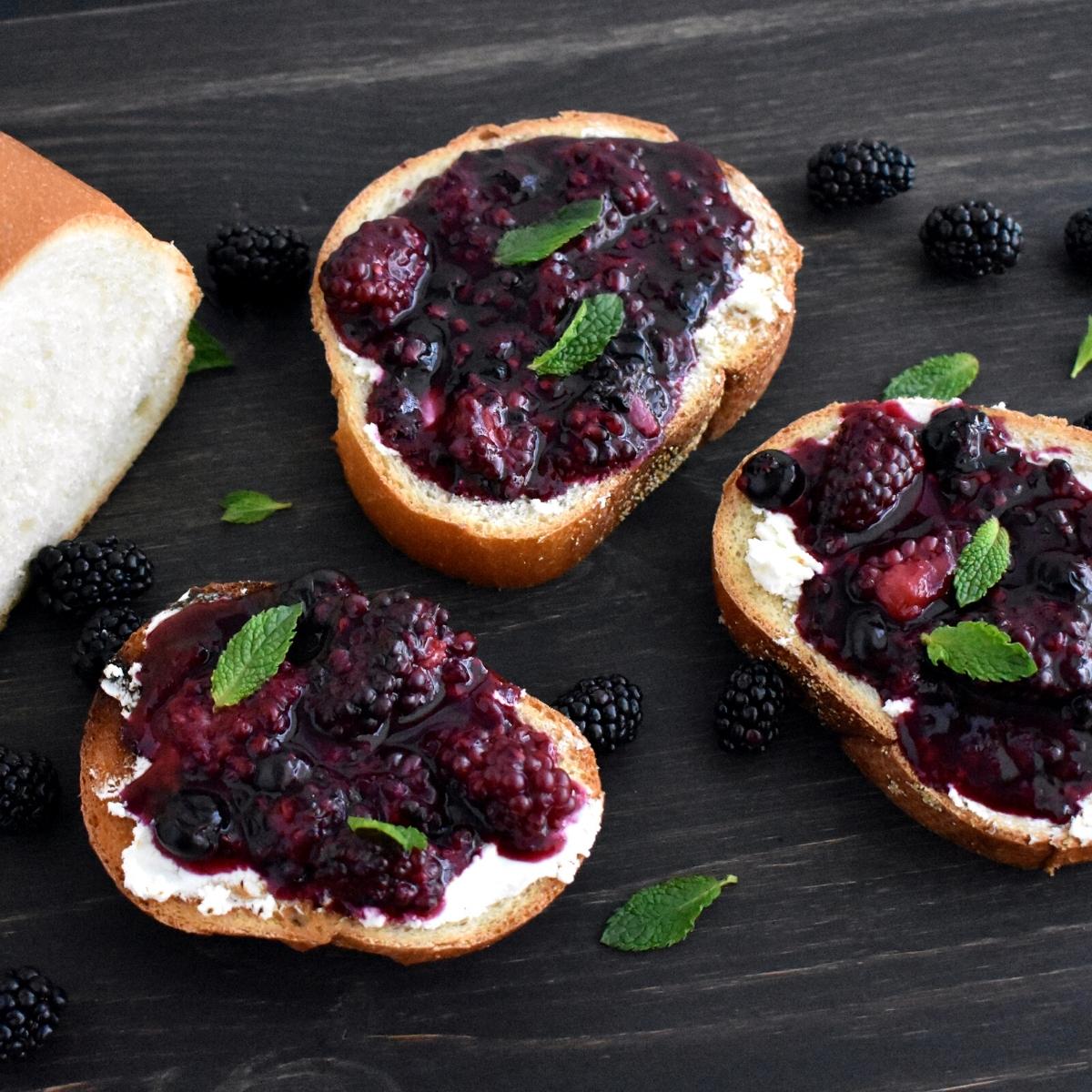 3 slices of goat crostini topped with white goat cheese and pickled blackberries. Garnished with green herbs on top.