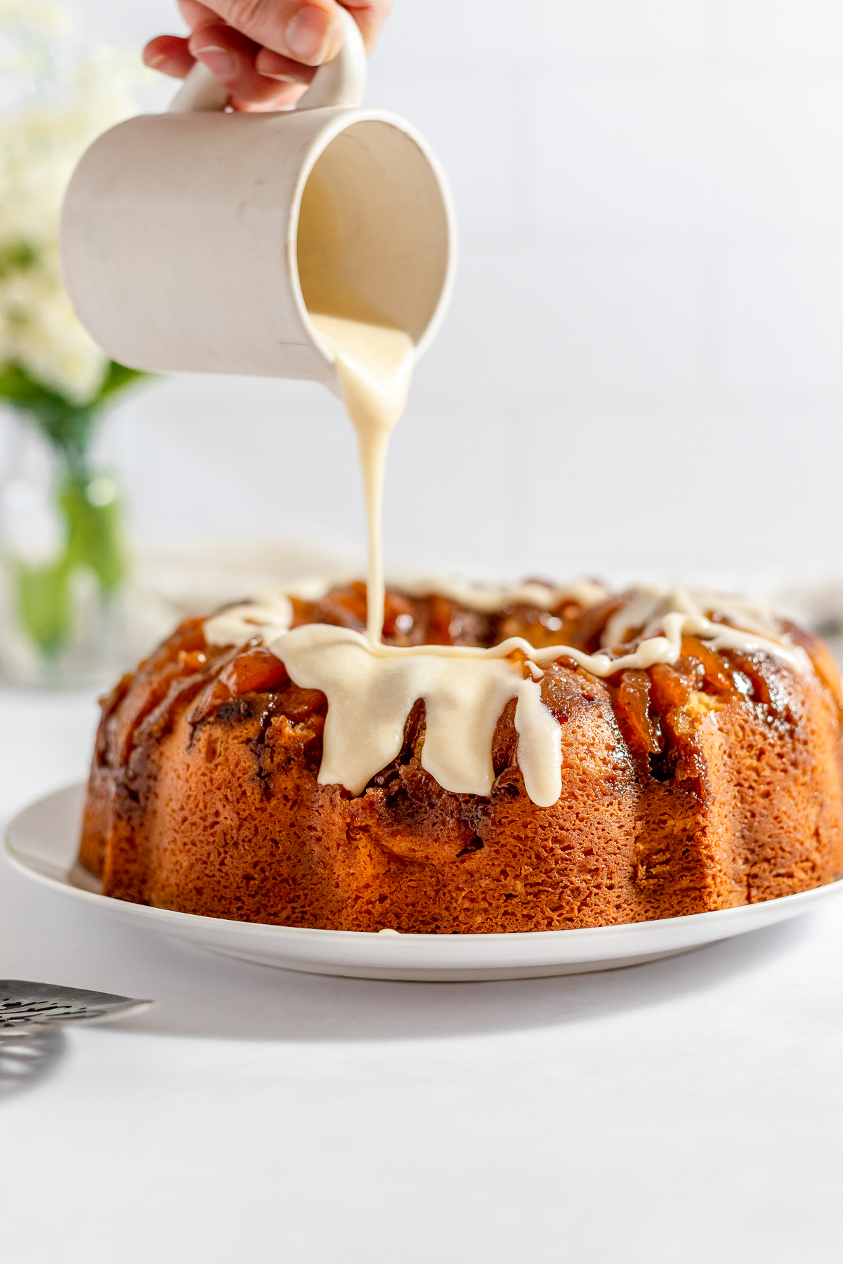 A light brown bundt cake with creamy icing being drizzled over the top.