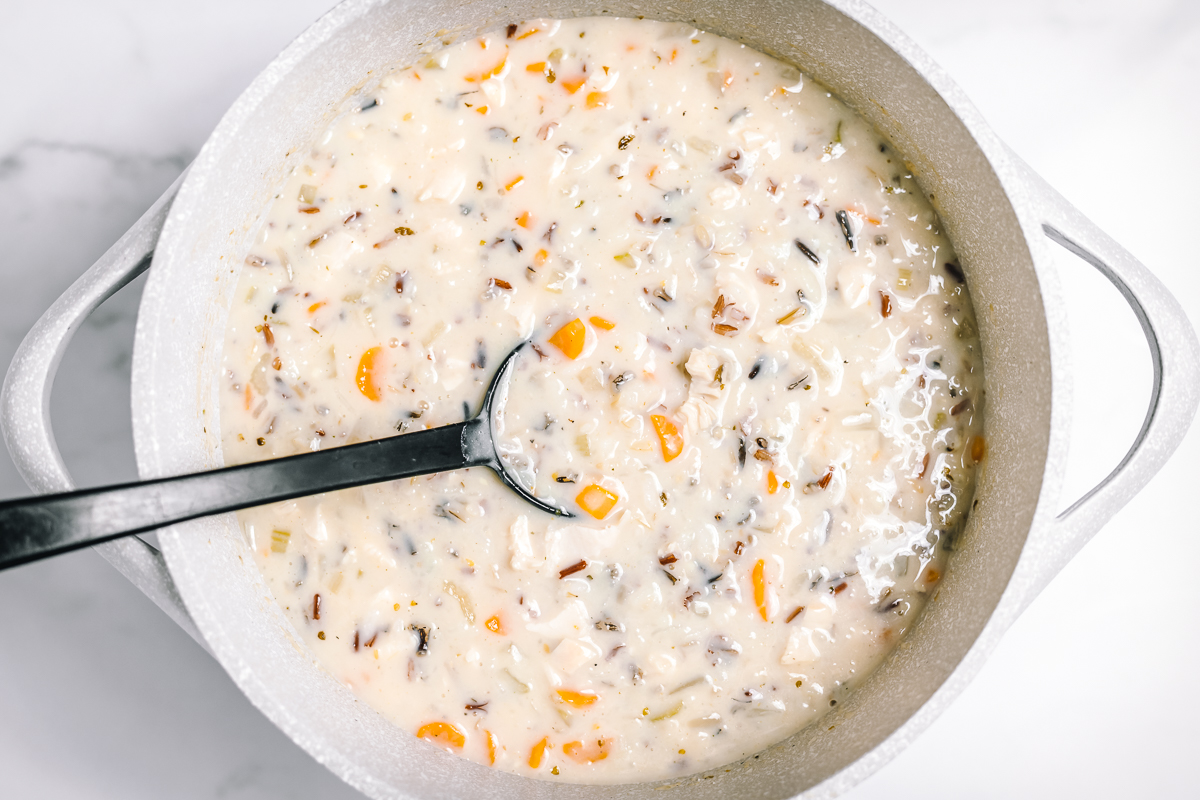 Chicken wild rice soup is now thickened. It is a creamy pale color with the chunky ingredients evenly distributed throughout it.