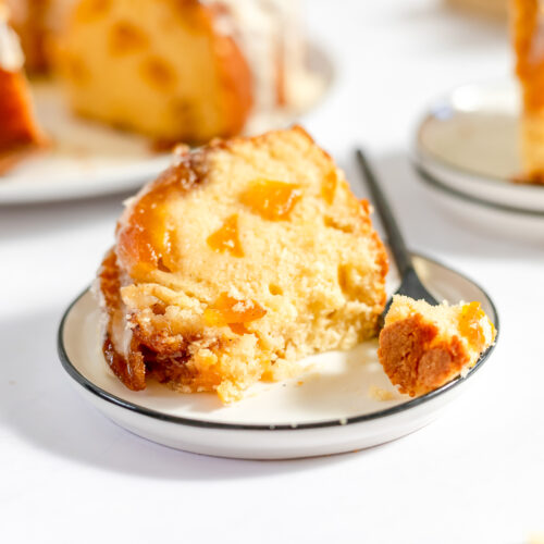 A slice of peach cobbler pound cake studded with yellow orange chunks of peaches and drizzled with thin white icing.