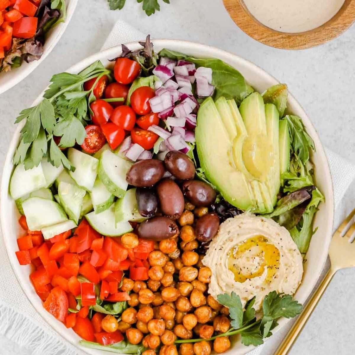 Buddha bowl filled with avocado, chopped veggies, olives and chickpeas.