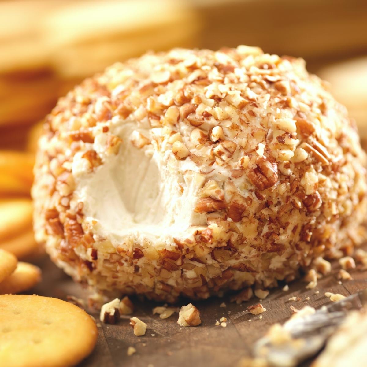 A crushed walnut coated cheeseball surrounded by round Ritz crackers.