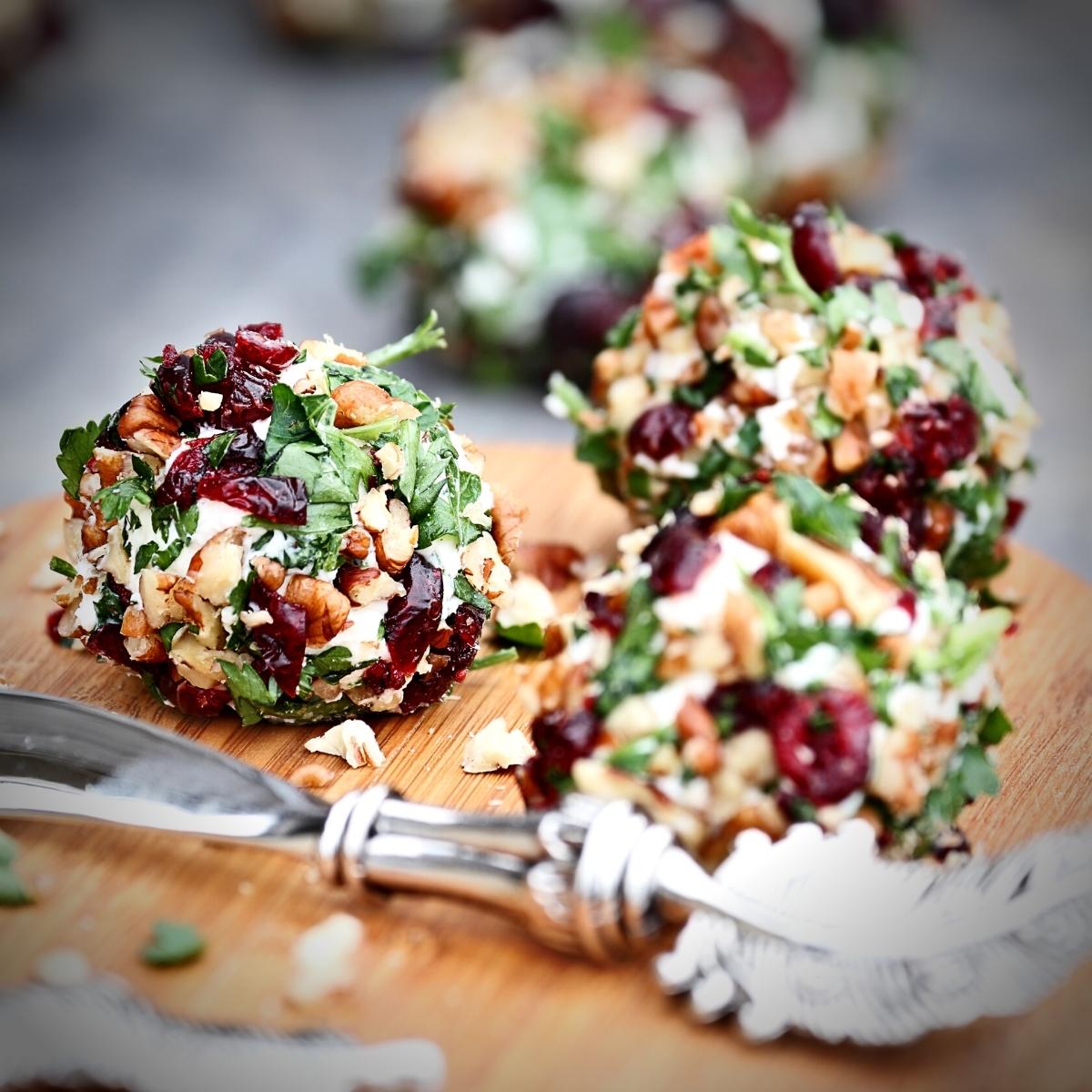 Colorful dried cranberry and parsley coated cheeseballs on a wooden platter.