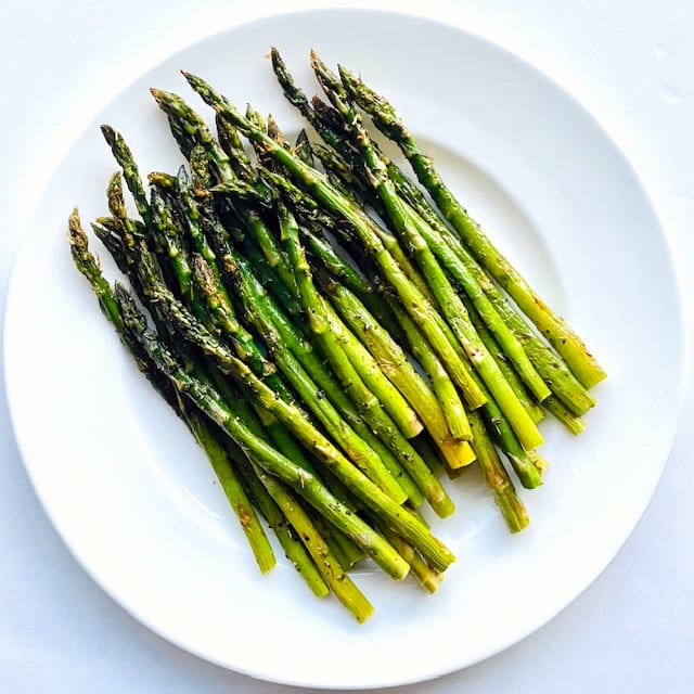 Grilled bright green asparagus on a round white plate.