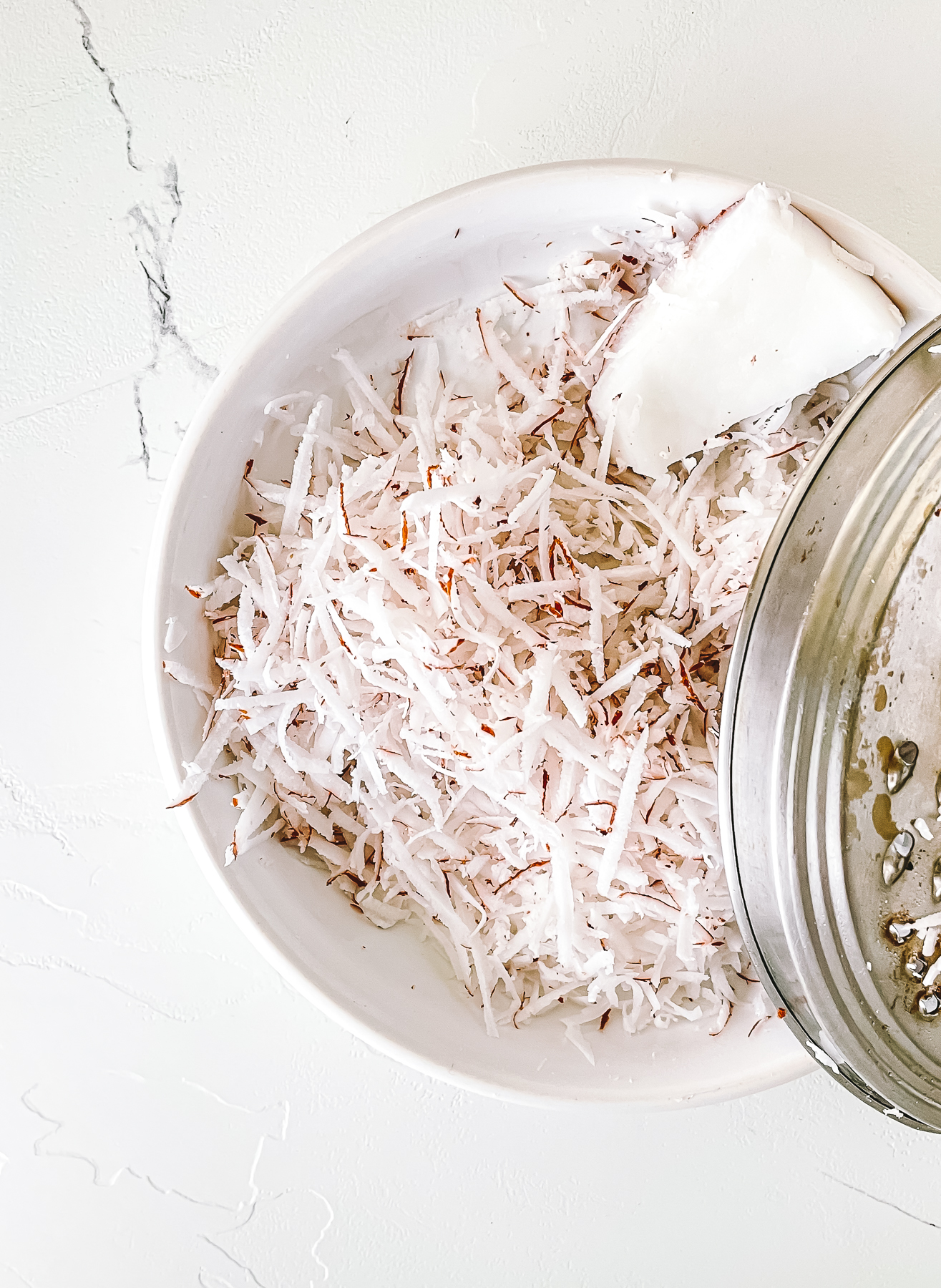 Shredded white coconut with bits of brown on the edges in a bowl with the grater beside it.