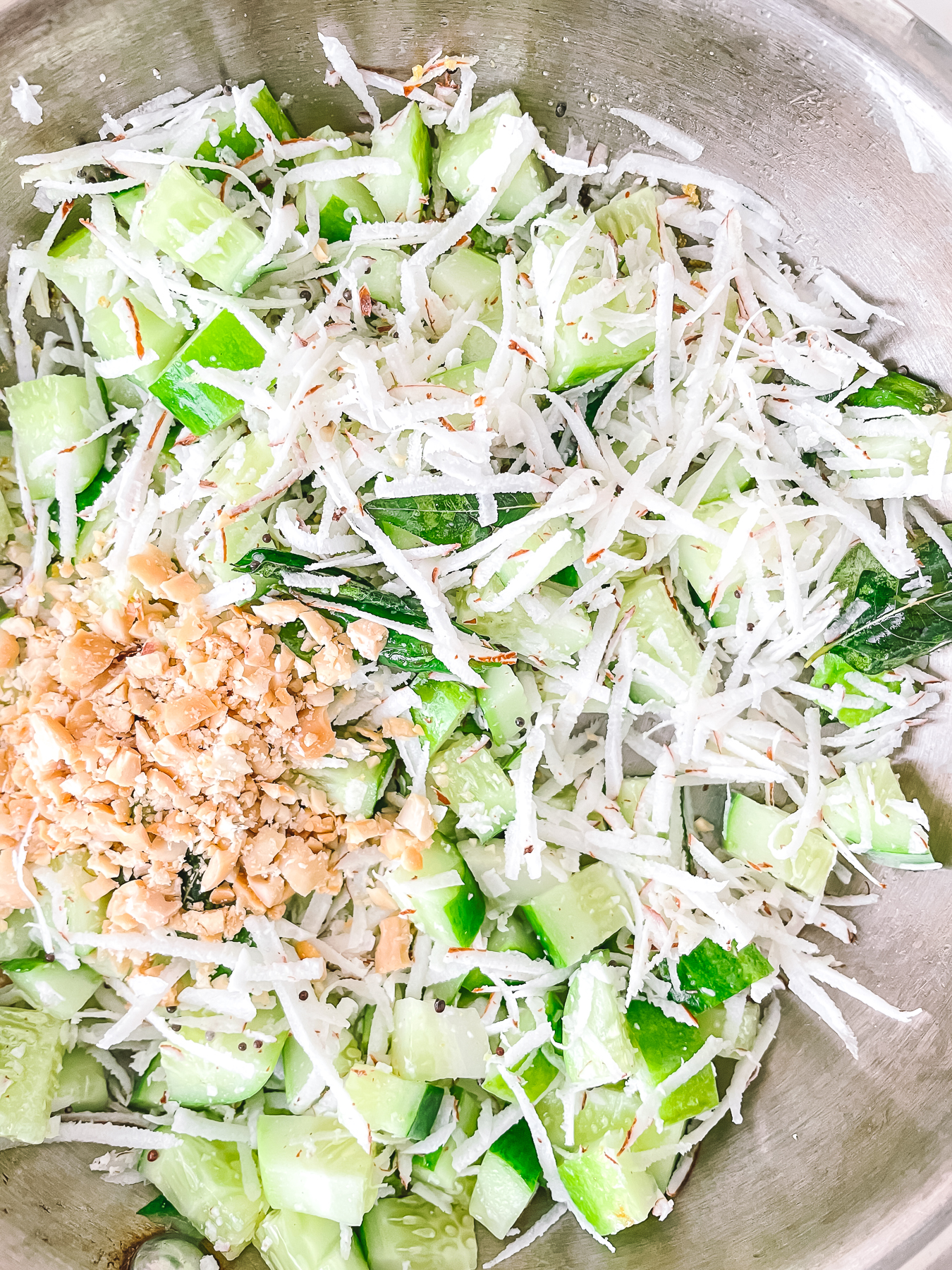 Cucumber chunks, shredded coconut and crushed peanuts poured into a metal bowl but not yet tossed together.