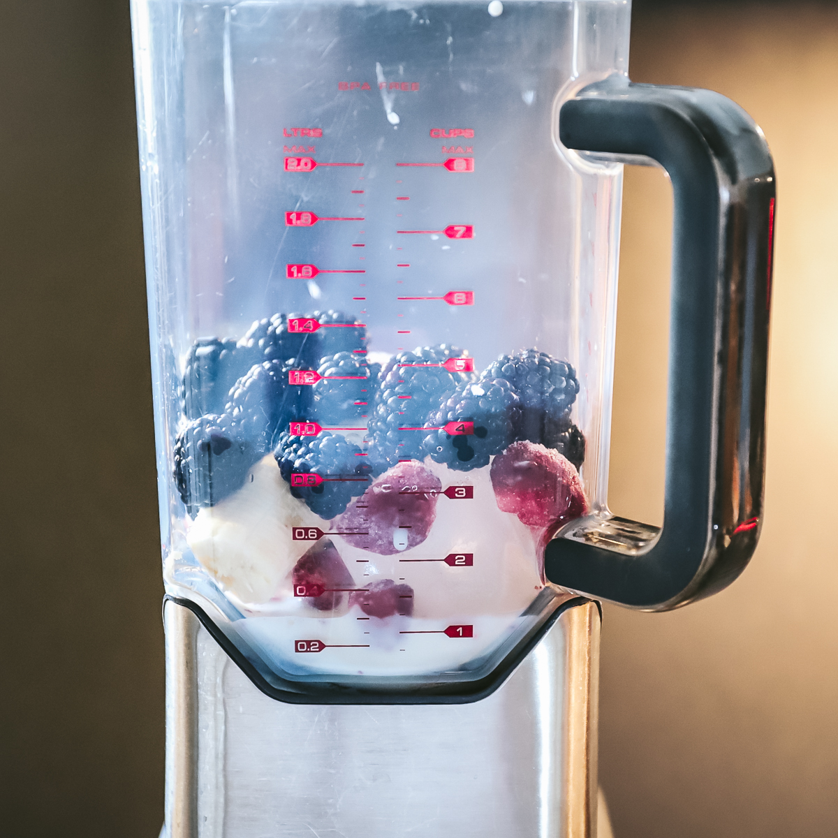 Smoothie step 1 has the bowl of a blender layered with white yogurt, banana, and berries.