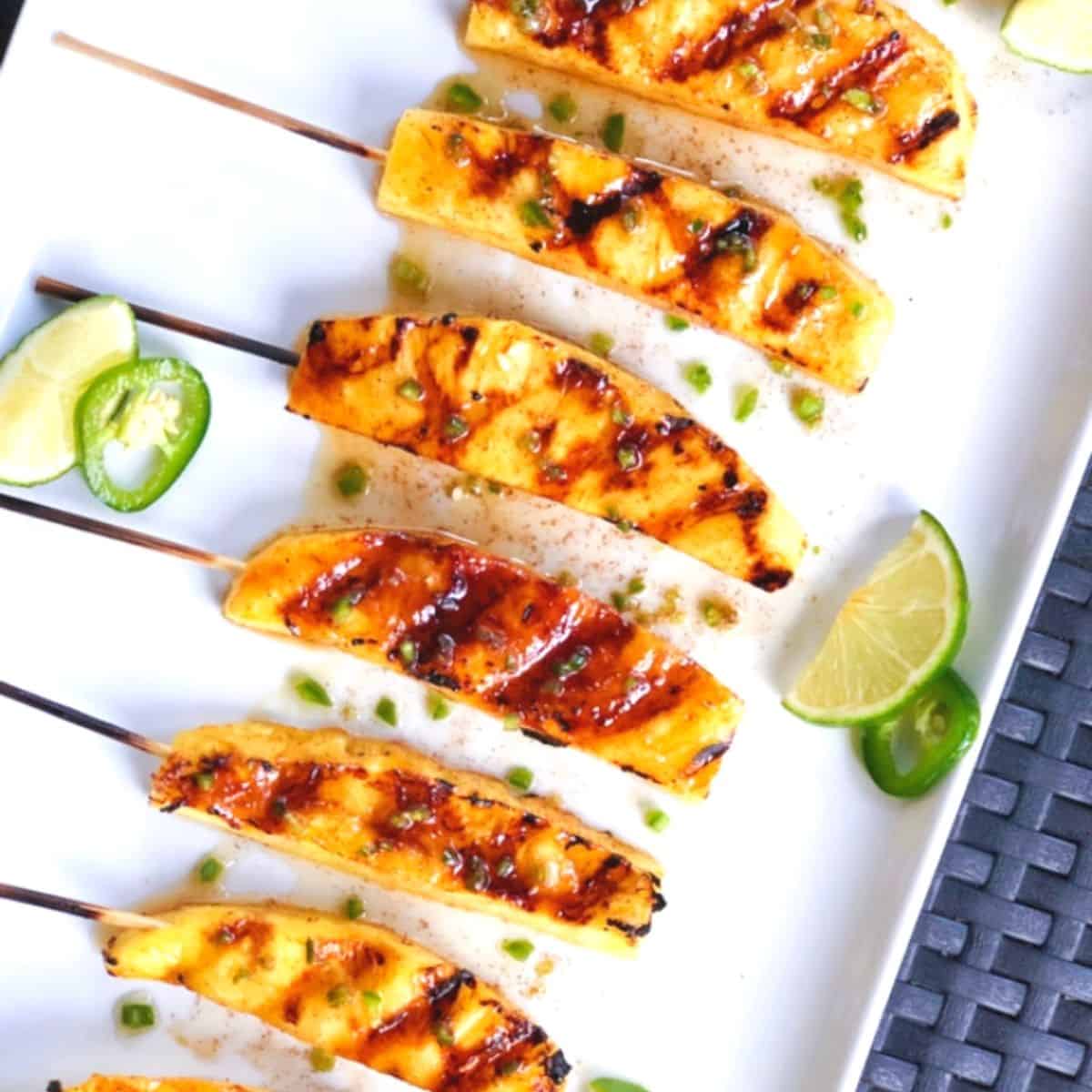 Grilled pineapple skewers on a white tray with lime wedges.