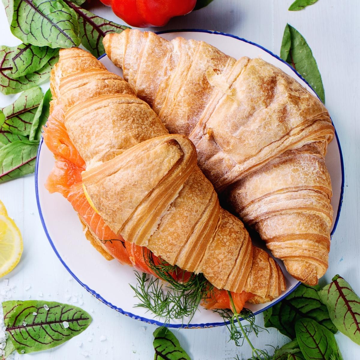 2 croissant sandwiches stuffed with red salmon and surrounded by spinach leaves.