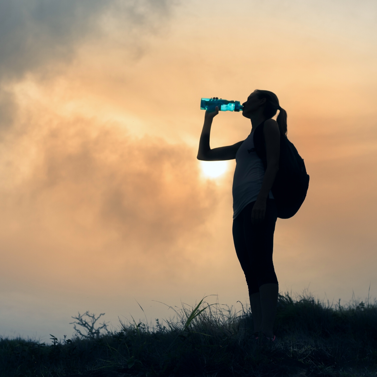 A lady on a ridge at dawn drinking water from a water bottle
