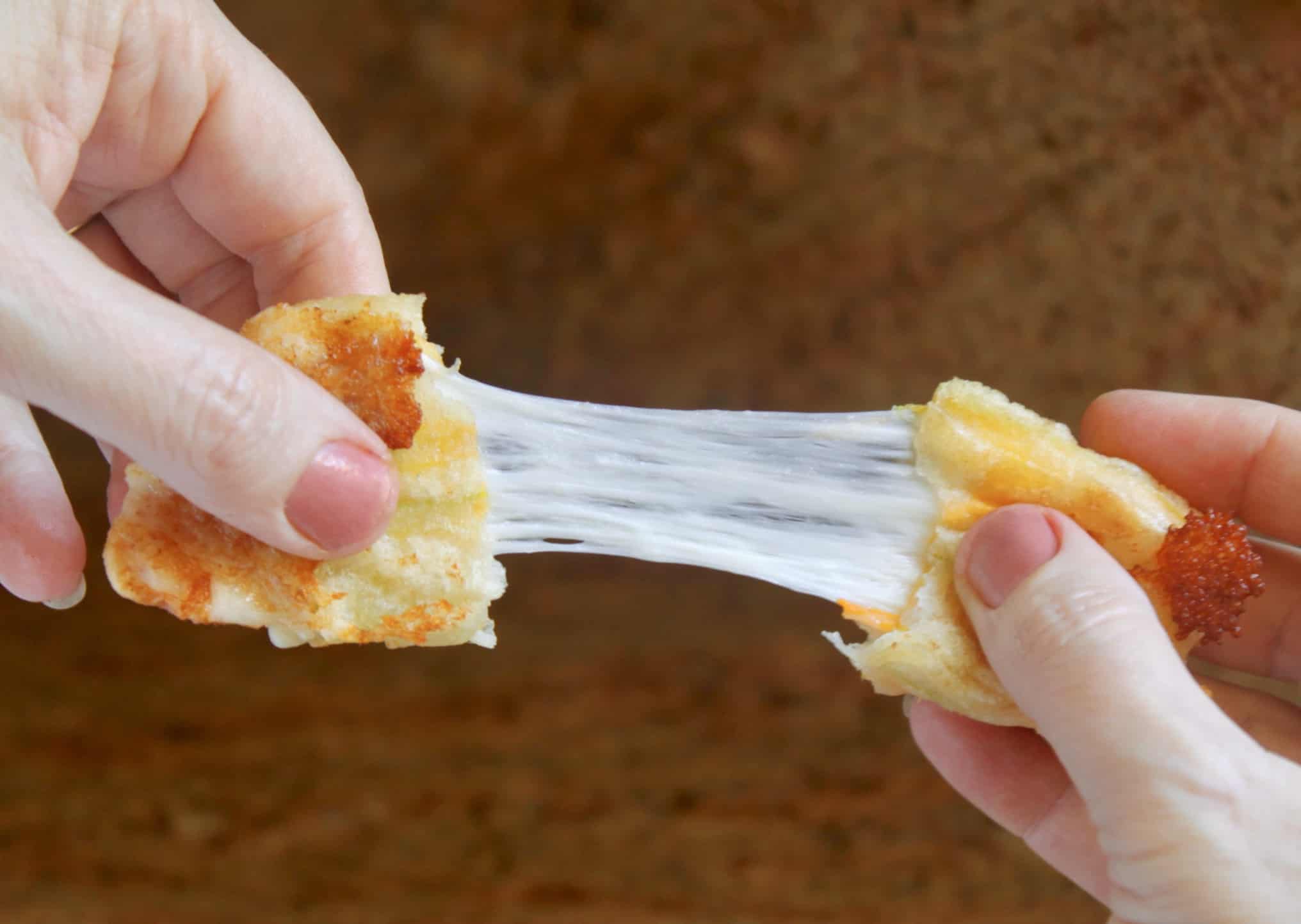 Crispy mozzarella cheese stick is being pulled apart by hands, showing the stretchy, melted cheese inside.