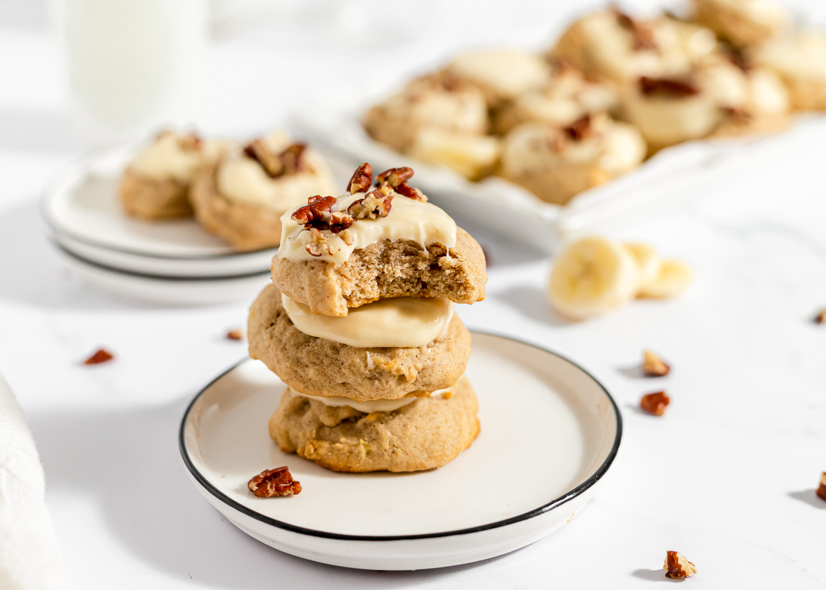 3 cookies stacked on a plate with slices of banana and chunks of pecan scattered around.