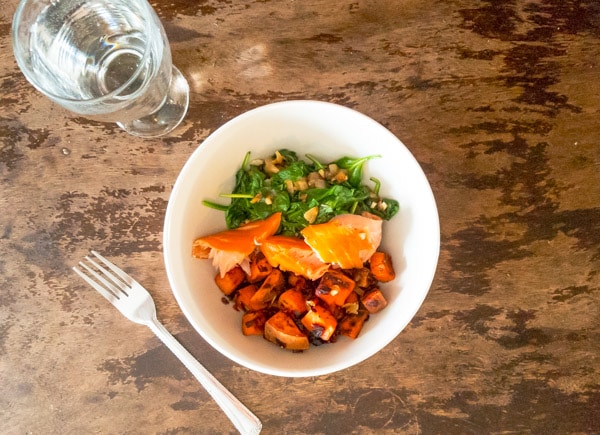 Bowl of cooked salmon chunks with greens and carrots.
