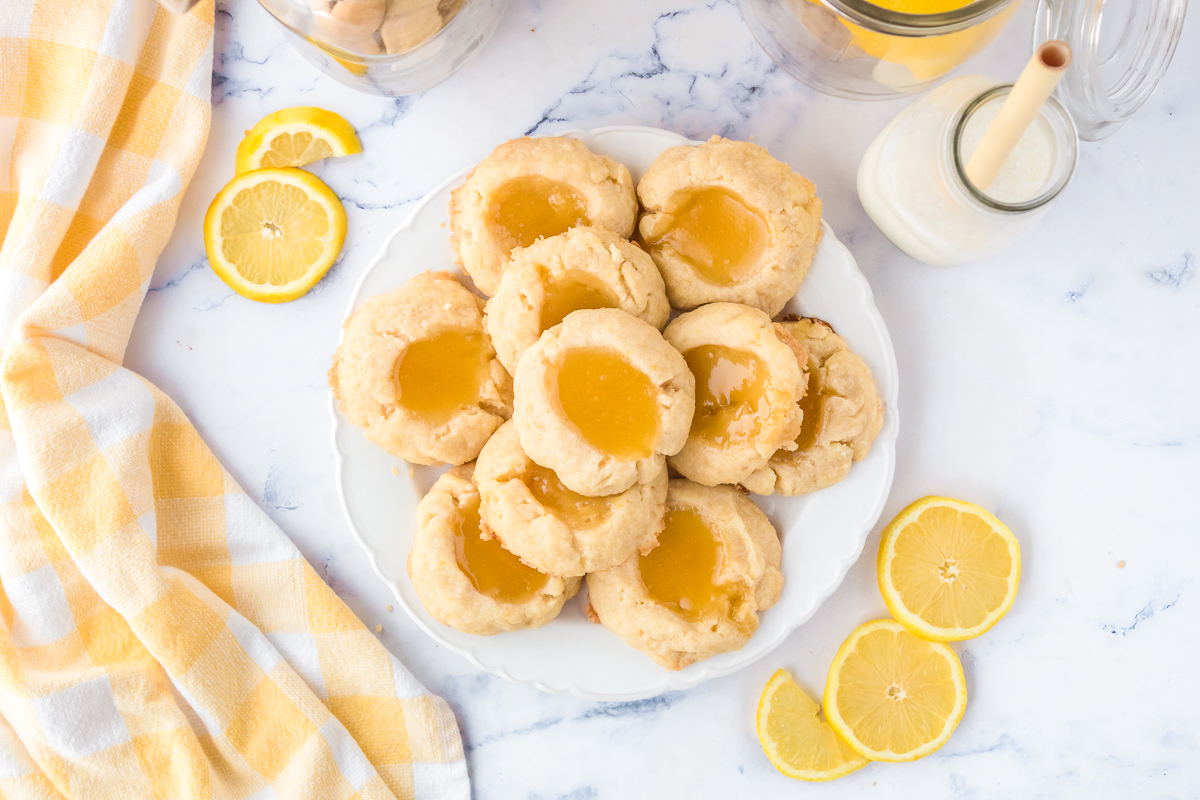 A round white plate of cream colored cookies with bright yellow lemon curd centers on a countertop.