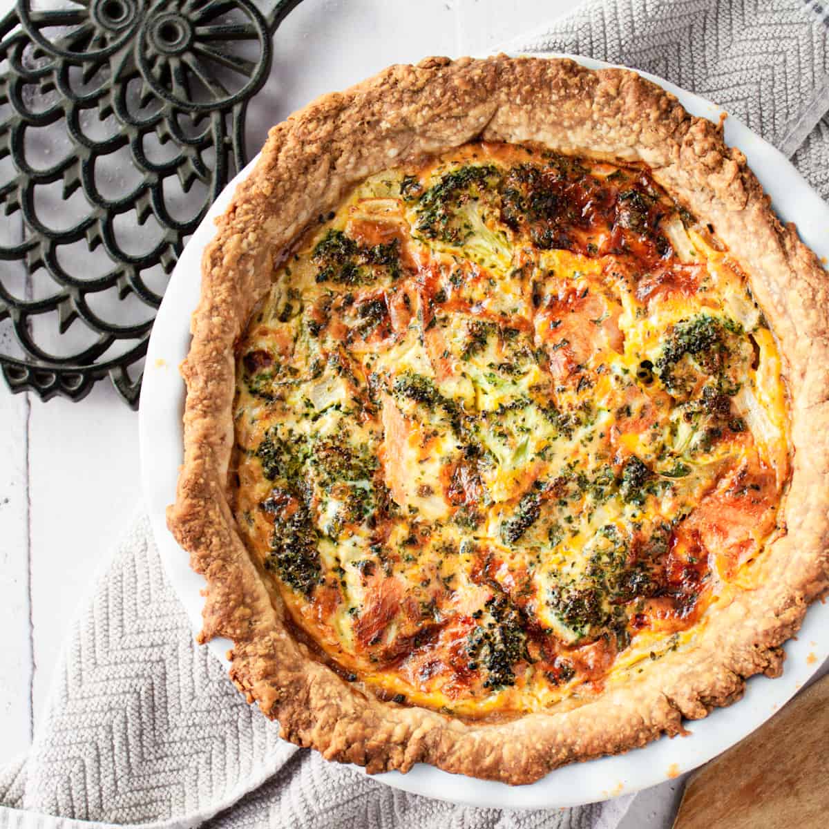 Salmon and broccoli quiche with a homemade, rustic looking pie crust in a white dish.