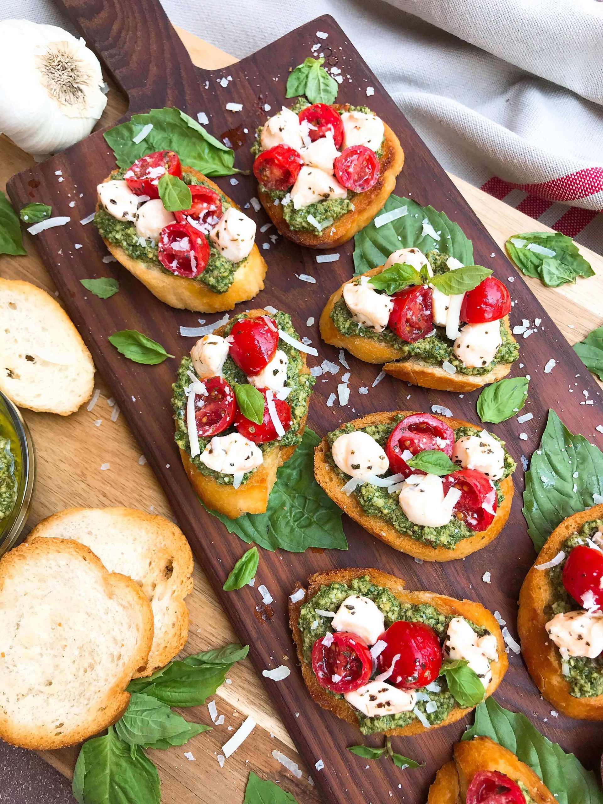 Bright colored bruschetta is topped with white cheese, red cherry tomatoes and green pesto.