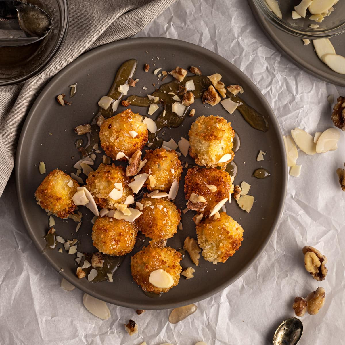 Crispy golden small cheese balls on a gray plate drizzled with syrup or honey and sprinkled with slivered almonds.