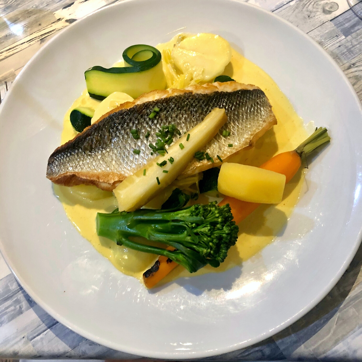 Cooked turnips and broccoli with seared fish and a pale yellow sauce.