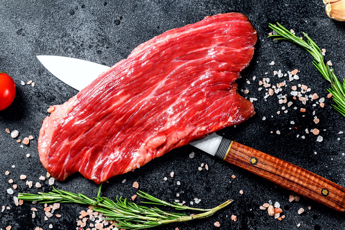 Raw steak on a black cutting board with a knife under it.