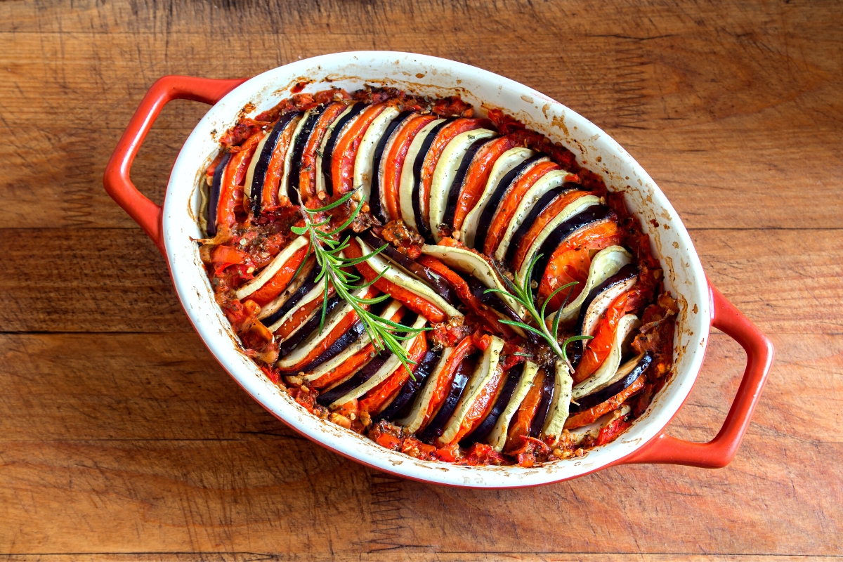 A classic ratatouille of sliced rounds of colorful vegetables arranged in a circular fashion in a oval casserole dish.