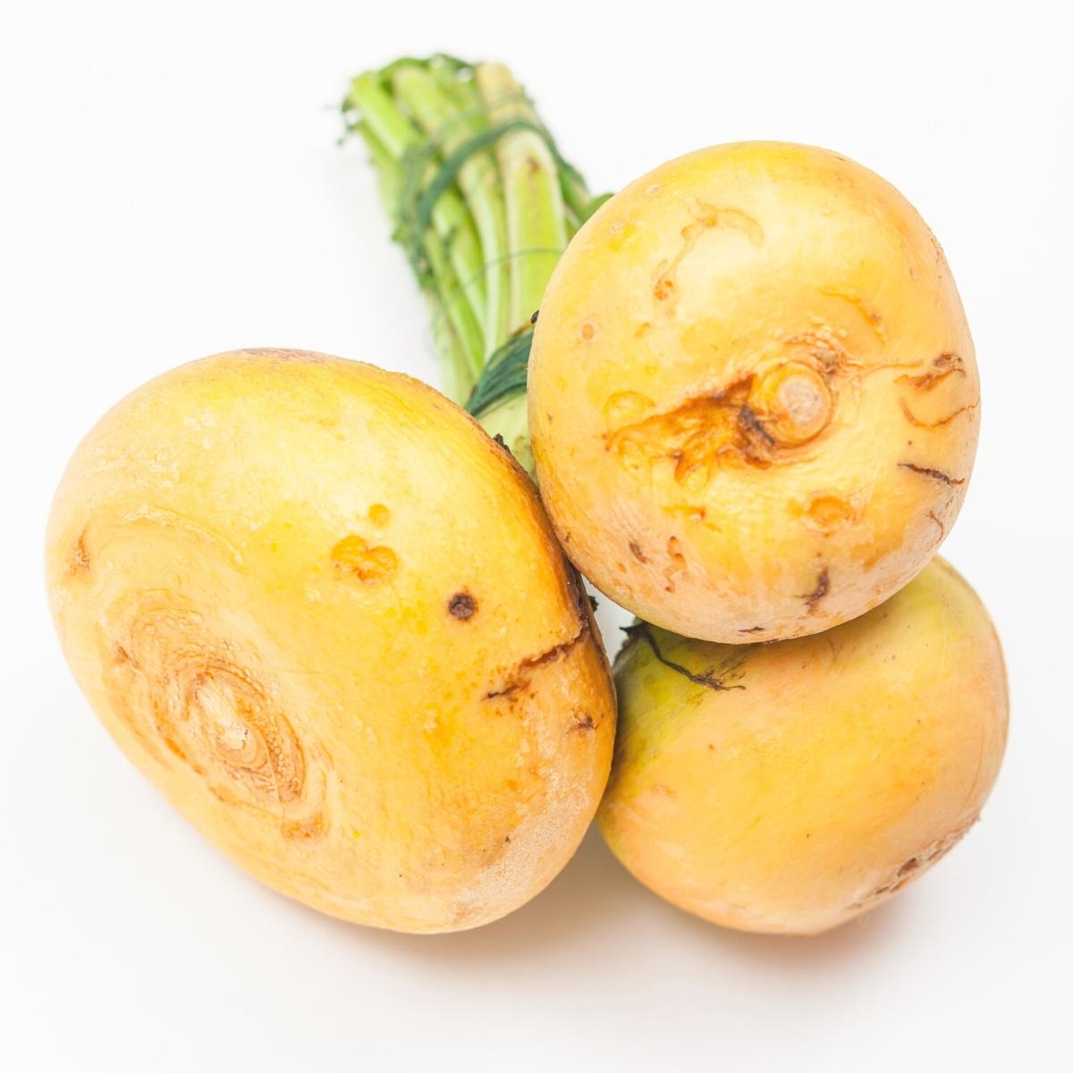 Yellow turnips with green stems attached and bundled.