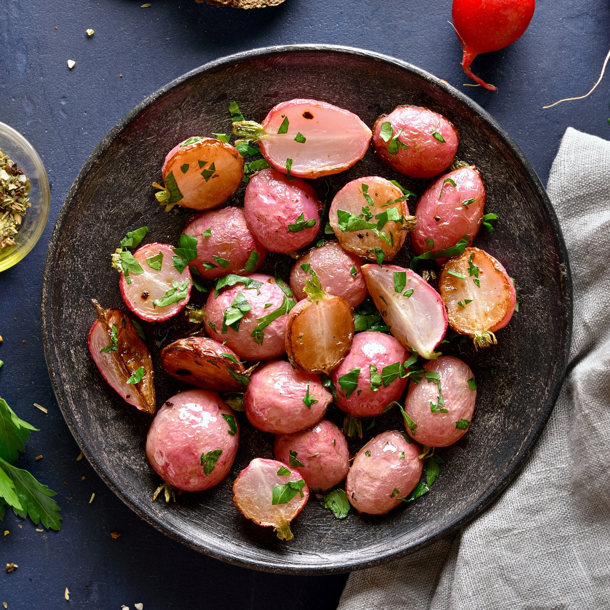 Muted red radishes that have been cooked and are served with chopped parsley in a black pan.