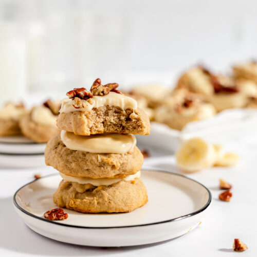 Three stacked banana bread cookies that are a very light brown color with creamy icing and nuts on top.