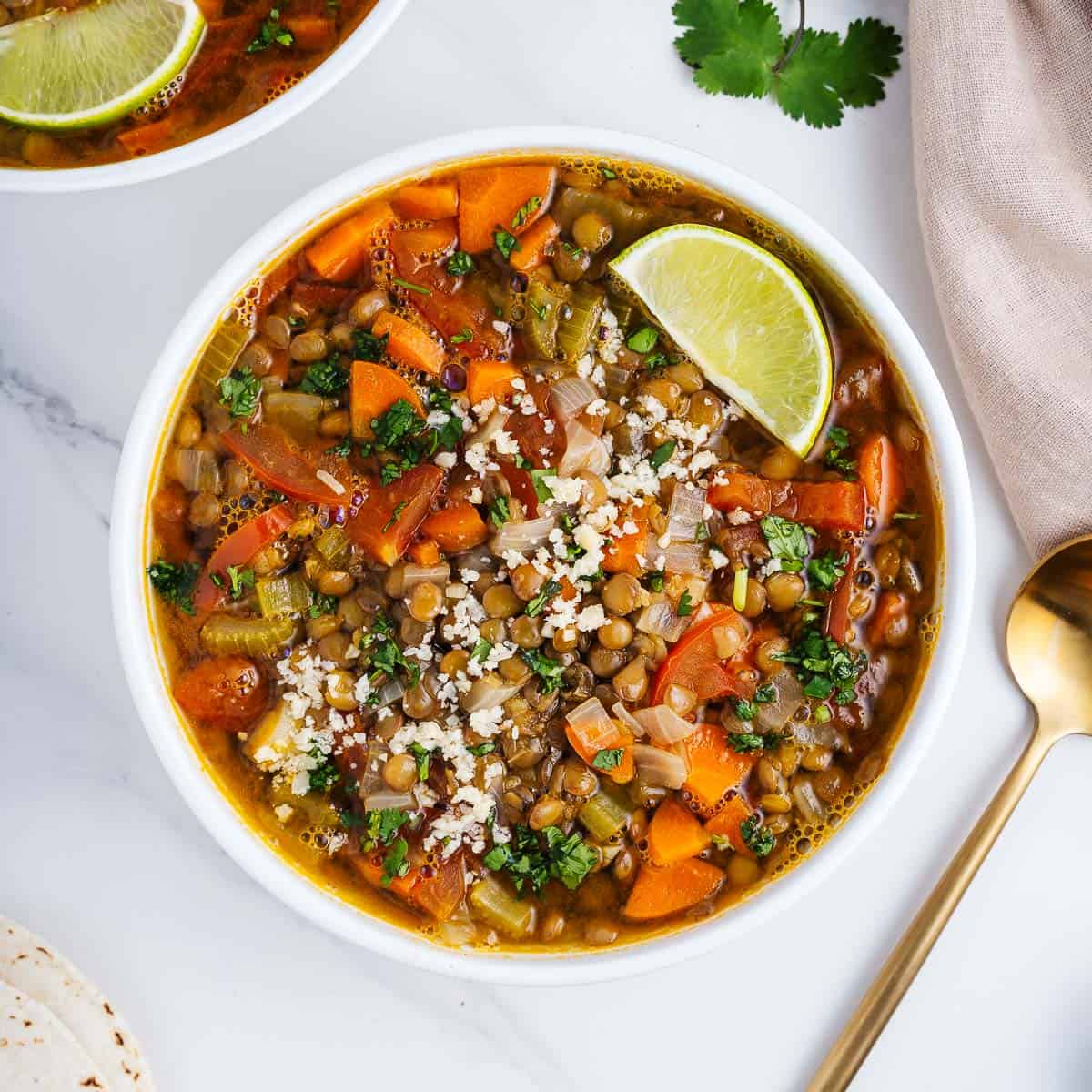Colorful soup of lentils with carrot, rice and cilantro garnished with lime wedge in a white bowl.