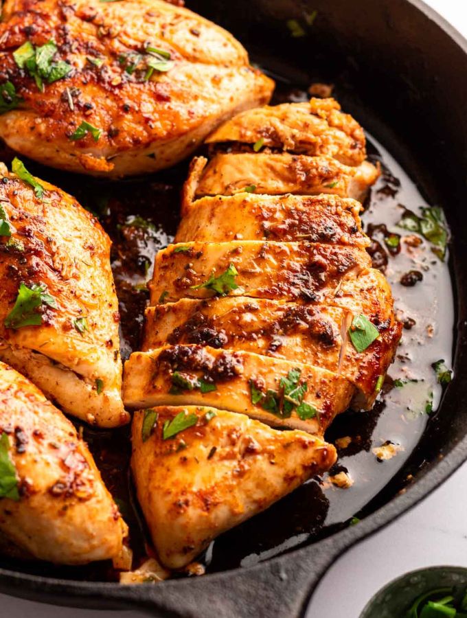 Golden brown chicken breasts in a black cast iron pan that have been sliced thinly but are still in the chicken breast shape.