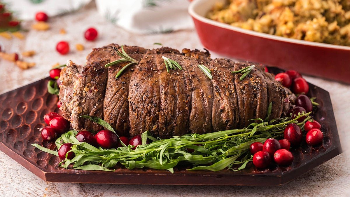 Rolled steak topped with cranberries and rosemary on a platter.