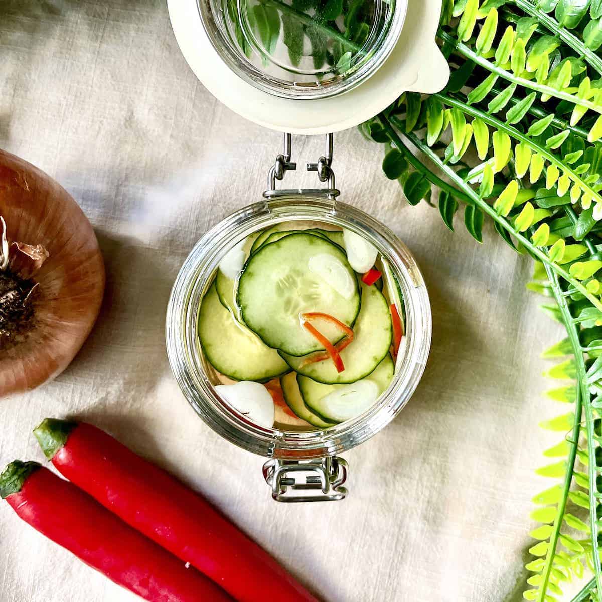 An open glass jar of fresh cucumber pickles with slivered red chili in it.