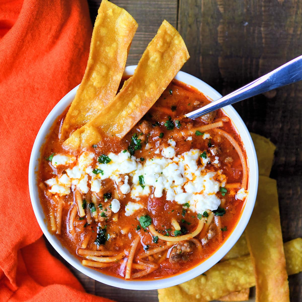 Mexican noodle soup is deep roasted red color with long thin noodles. It is garnished with crumbled white cheese and some tortilla strips.