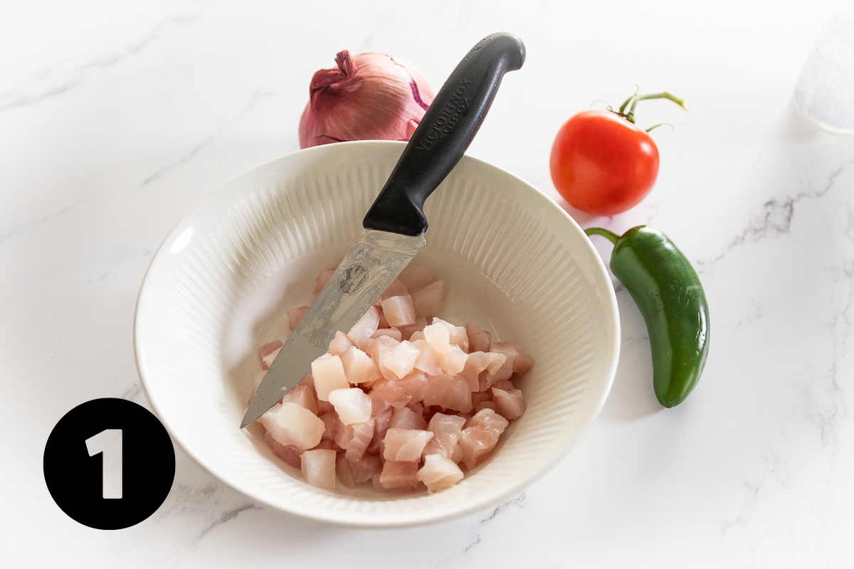 White fish sliced into ½ inch cubes in a white bowl with sharp knife beside.