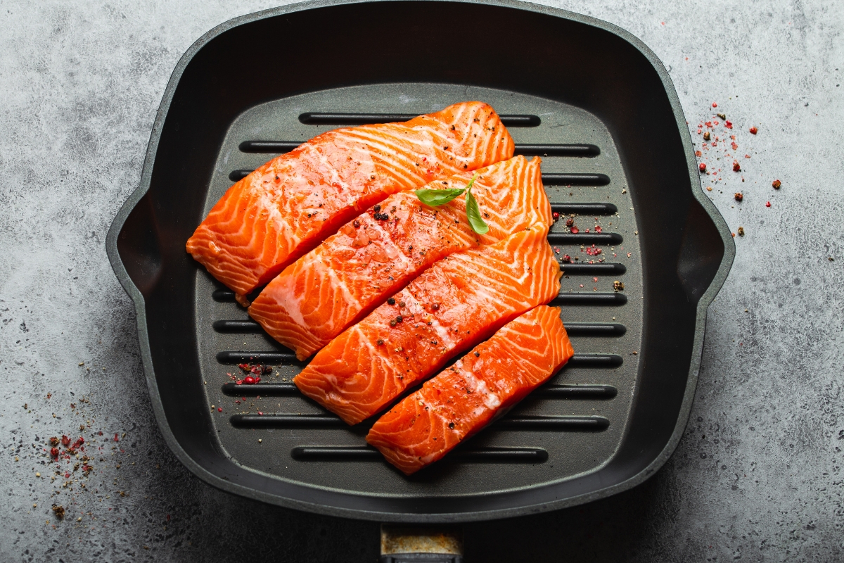A cast iron grill pan with a fillet of salmon cut into 4 equal pieces.