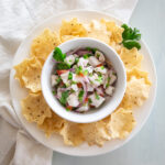 Round bowl of cupped tortilla chips with a bowl of white, red, green and purple ceviche in the middle.