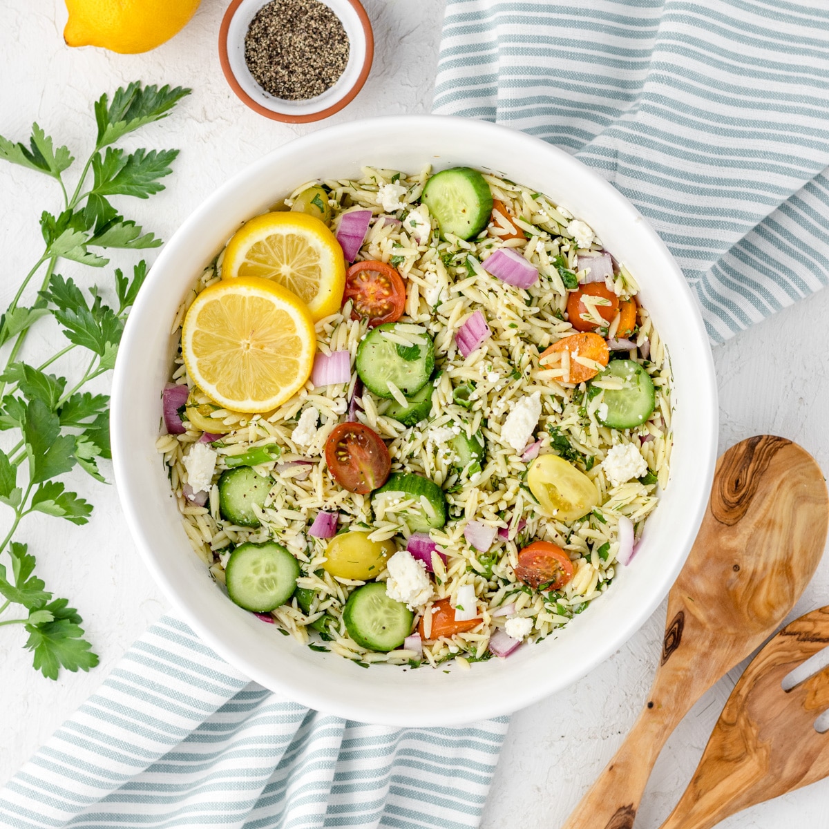 Colorful salad of small orzo pasta with lemon, chopped tomatoes, cucumber and parsley with lemon slices garnishing the side.