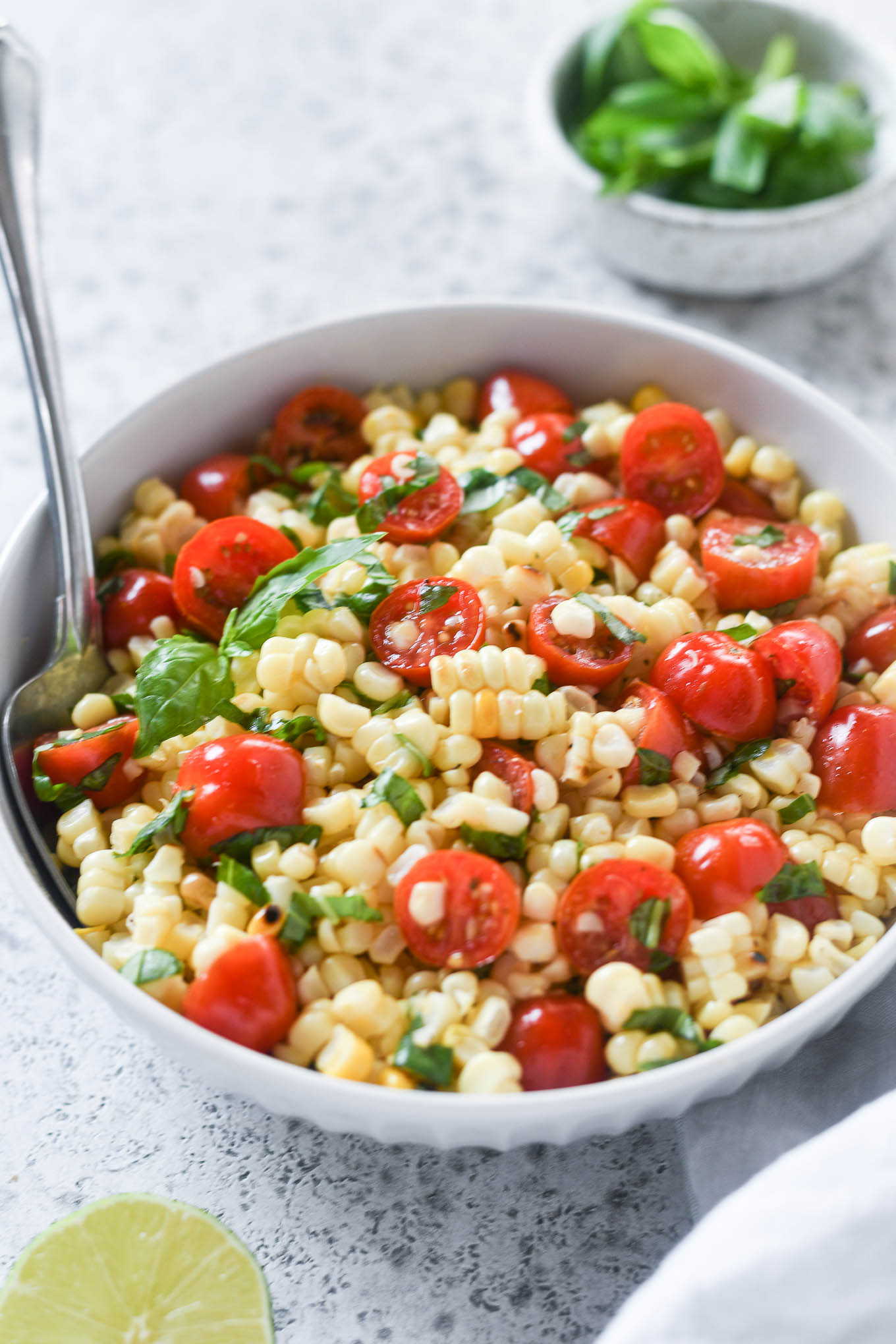 Yellow corn and red tomato salad with chopped green herbs in a white bowl.