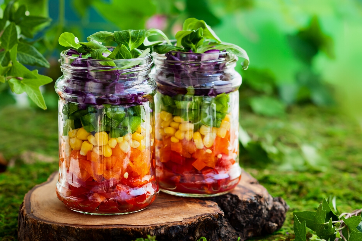 Two mason jar salads arranged with layered veggies in the order of the rainbow.