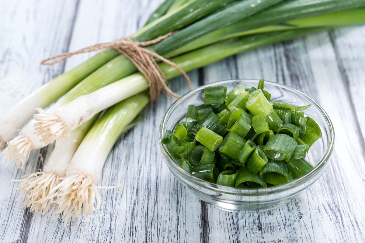 A bunch of green onions with white bases and a small glass dish of chopped green onions.