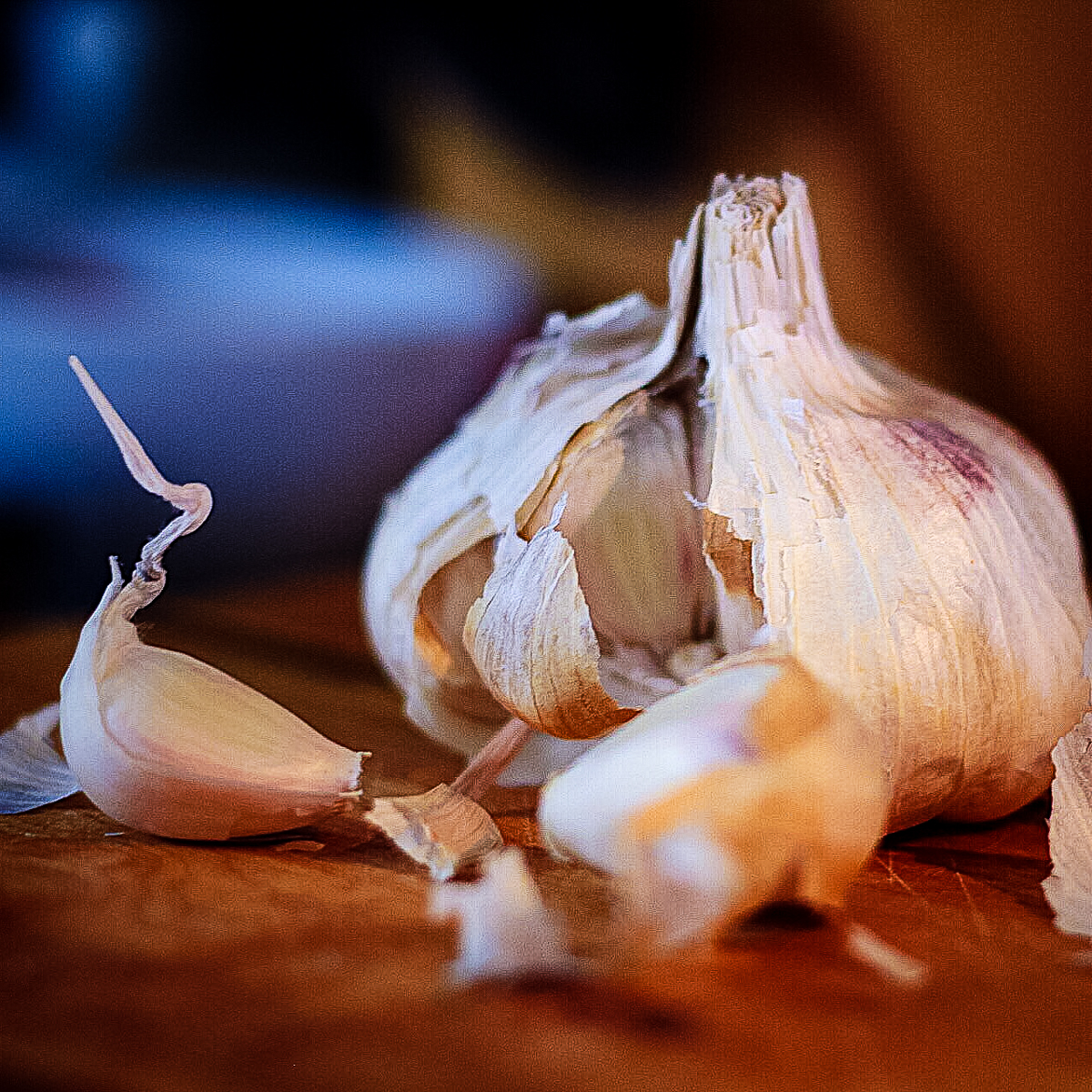 A bulb of garlic with the papery husk peeled back on one side and 2 garlic cloves pulled out and laying beside.