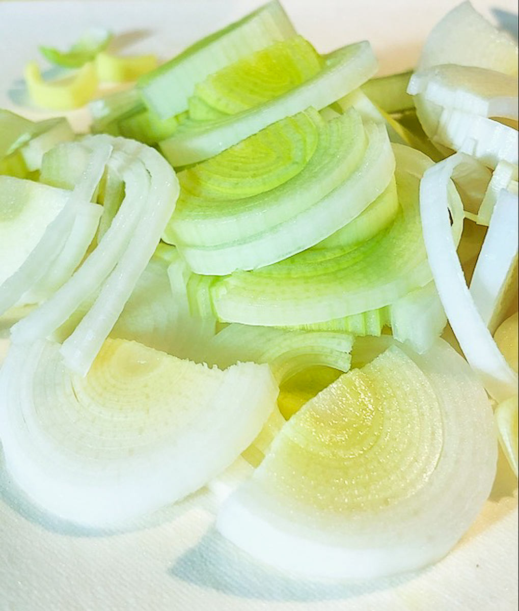 Sliced pale green and white parts of a leek. The slices are round with many concentric layers.