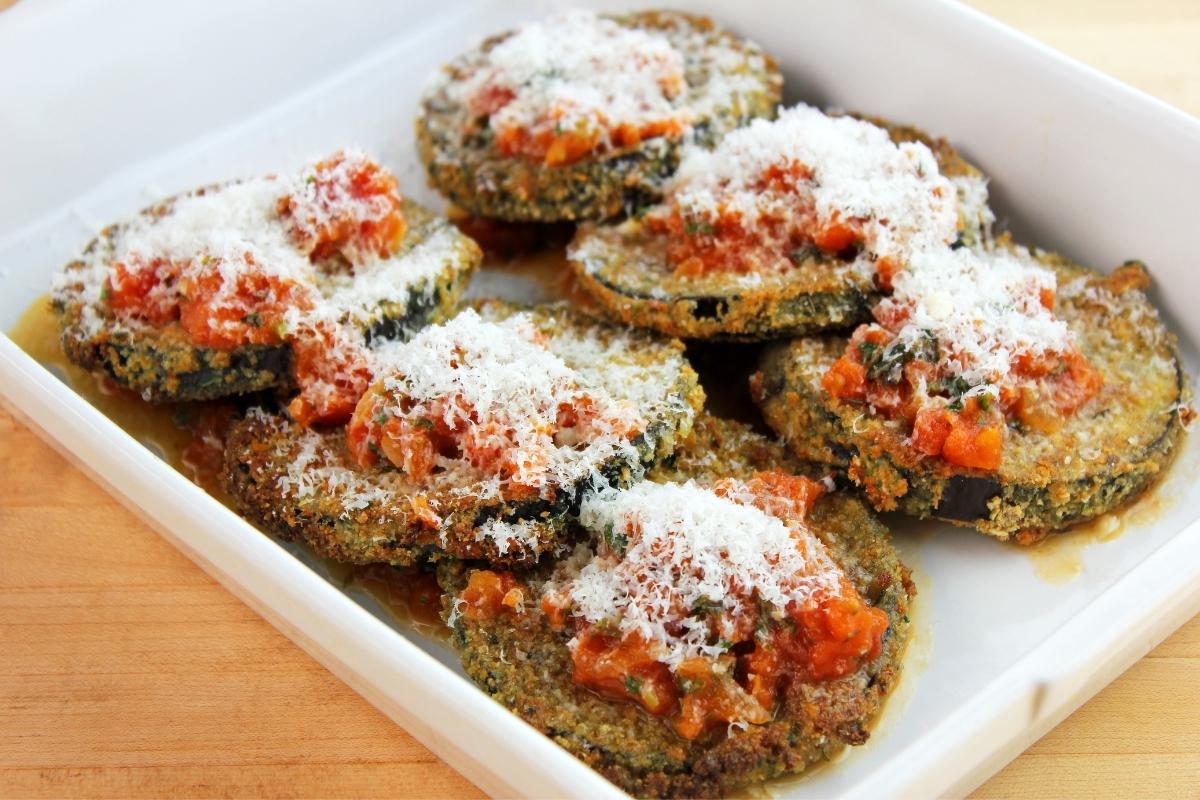 White shredded parmesan cheese on top of eggplant parmesan with tomato sauce in a white casserole dish.