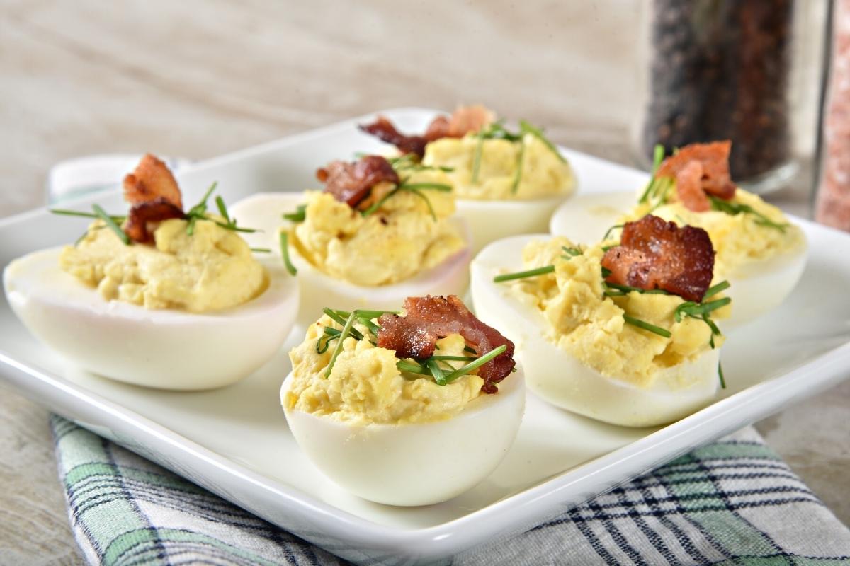 Devilled eggs topped with bacon and chives on a plate.